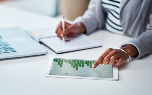 Shot of an unrecognizable businesswoman using a digital tablet with graphs on it in a modern office