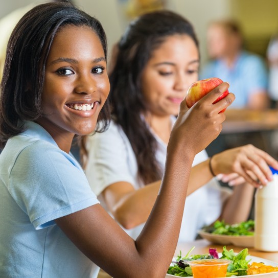 Teenager eating healthy lunch with friends in school lunchroom