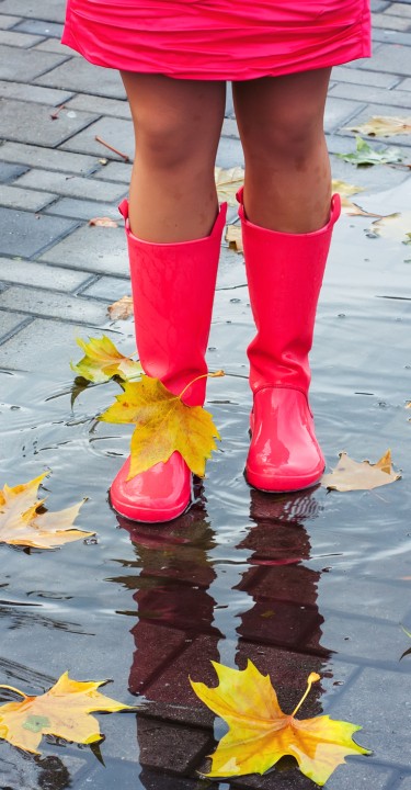 Woman with pink rubber boots splashing in a puddle after rainfall