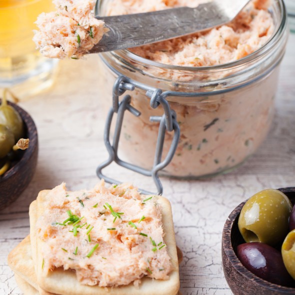 Smoked salmon and soft cheese spread, mousse, pate in a jar with crackers, olives and capers on a wooden background