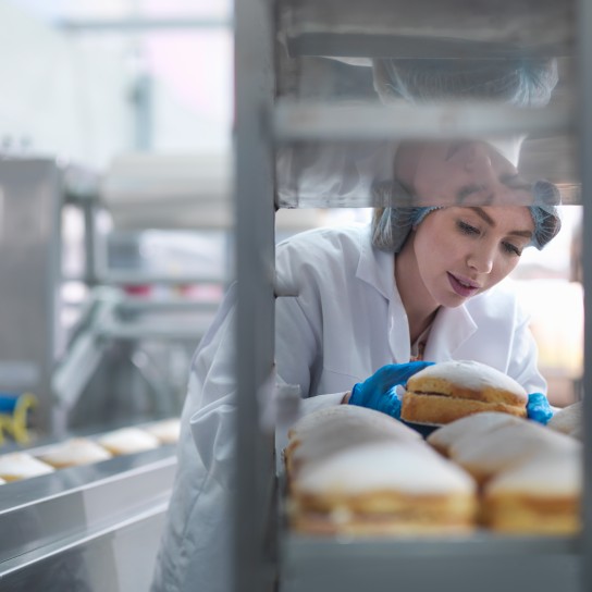 Female baker putting cakes on packaging line in cake factory