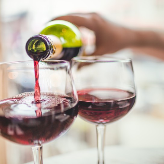 Unrecognizable man pouring red wine in two glasses.