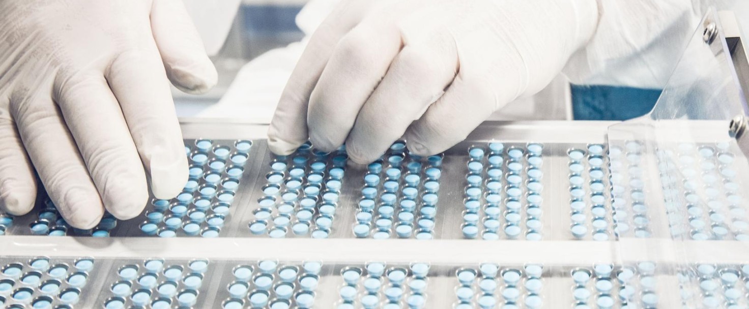 Worker inspecting pills on blisterpack conveyer belt