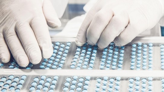 Worker inspecting pills on blisterpack conveyer belt