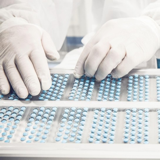 Worker inspecting pills on blisterpack conveyer belt