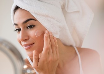 Woman with hair in towel rubbing lotion on face