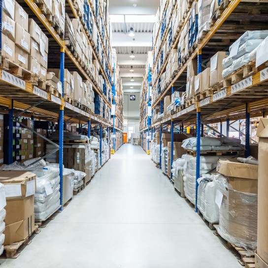 Horizontal color image of corridor in distribution warehouse in large factory. Storage room with shelves and racks arranged in a row. Boxes and crates of large warehouse factory ready to be delivered. Logistics, freight, shipping, receiving.