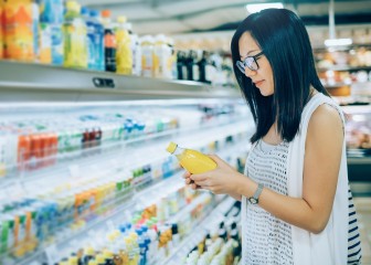Young woman reading carefully the nutrition labels on a bottle of beverage in a supermarket.