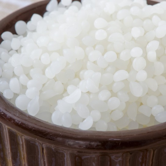 Close up of beeswax pellets in a brown ceramic bowl.