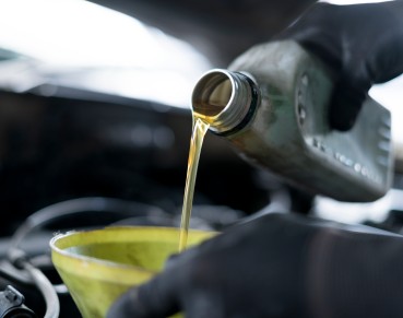 Close up of hand car mechanic refueling and pouring oil fill the oil in the engine, maintenance, and performance in auto repair shop.