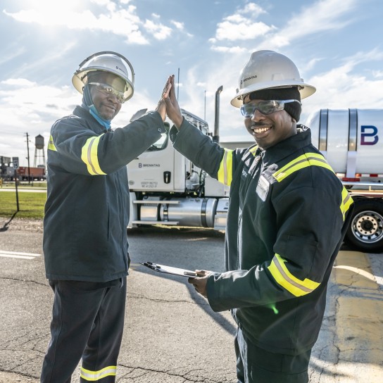 To mænd, der står foran en Brenntag-lastbil, giver hinanden et ‘high five’-håndtryk