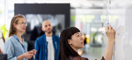 Young businesswoman explaining a business plan to colleague in office. Woman writing on the whiteboard during presentation in hybrid office space.
GettyImages-1327494174.jpg