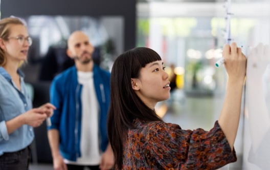 Young businesswoman explaining a business plan to colleague in office. Woman writing on the whiteboard during presentation in hybrid office space.
GettyImages-1327494174.jpg