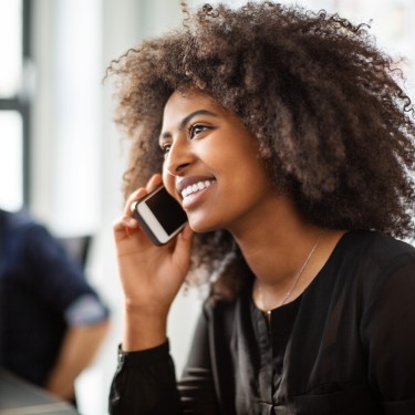Smiling african woman talking on phone. Female professional using cell phone while working at her desk.
GettyImages-1146500497.jpg