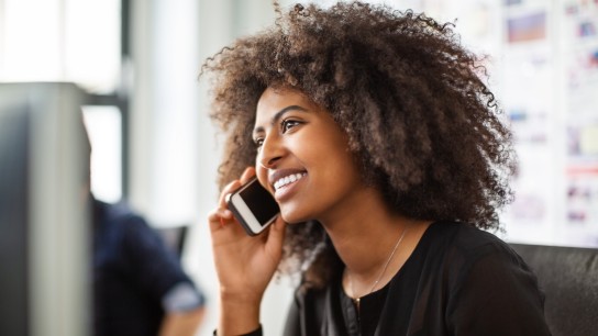 Smiling african woman talking on phone. Female professional using cell phone while working at her desk.
GettyImages-1146500497.jpg