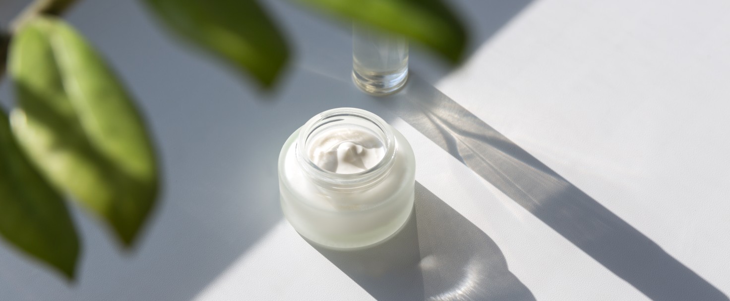 Cosmetic cream and serum, flower leaves. Natural hard light, deep shadows.