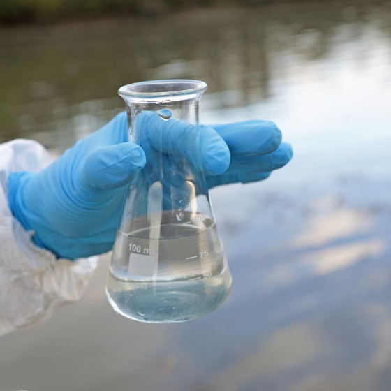 hand with protective clothing holding a flask of water above lake
GettyImages-1337888908.jpg