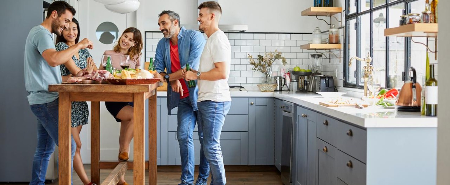 Happy males and females looking at friend with meat. Men and women are enjoying food together in kitchen. They are at home.
GettyImages-1374649188.jpg