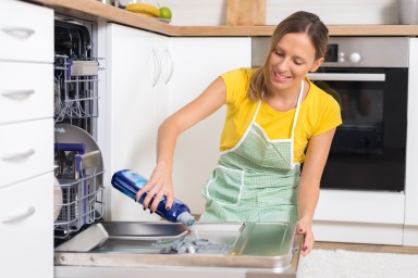 Happy young woman putting detergent in dishwasher