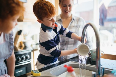 Two children and their Mother washing the dishes in the kitchen sink.