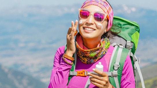Hiker woman applying sun cream to protect her skin from dangerous uv sun rays high in mountains. Travel healthcare concept