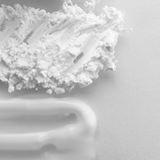 Close-up smear moisturizer and translucent loose powder on white background with copy space. Skin care concept, top view