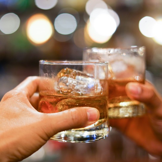 two men clinking glasses of whiskey drink alcohol beverage together at counter in the pub
