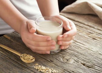 Young adult hands holds drinking glass with organic oat milk . Healthy eating lactose free milk substitute concept .Close up,selective focus.