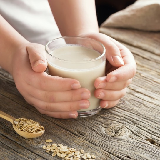 Young adult hands holds drinking glass with organic oat milk . Healthy eating lactose free milk substitute concept .Close up,selective focus.