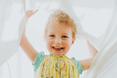 Playful young girl happily playing under a large clean white sheet. Laughing and hiding. Conceptual with space for copy.