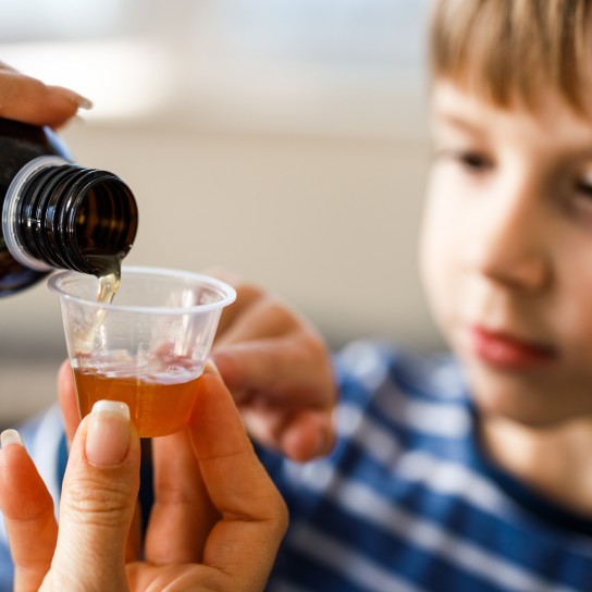 Close up of unrecognizable mother pouring cough syrup into a dose for her small boy at home.