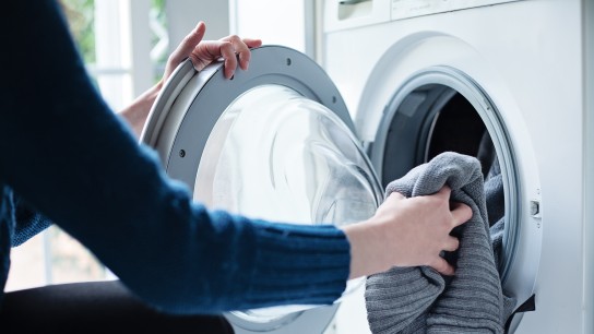 Woman’s hand loading dirty laundry in a white washing machine