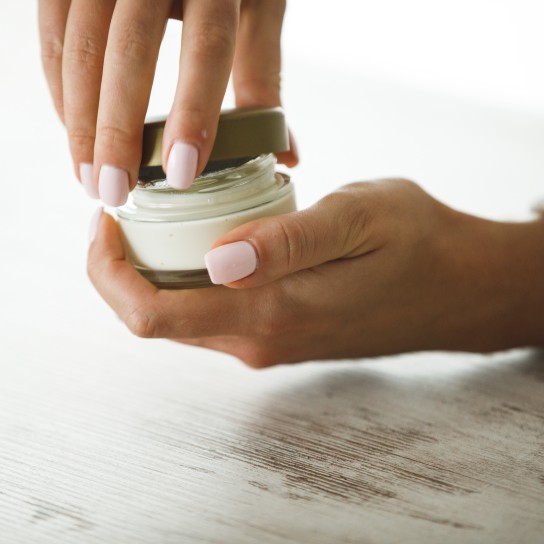 Close up of female hands opening a small round jar of cream by twisting the lid before using it to moisturize skin.