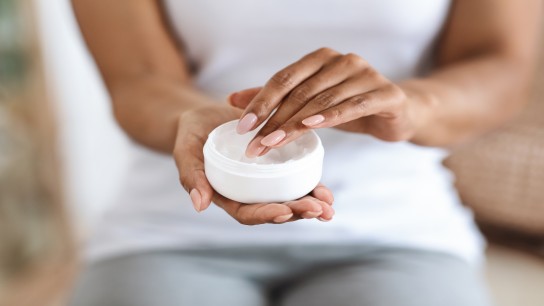 Unrecognizable Black Woman Holding Jar Of Moisturizing Cream, Doing Beauty Treatment At Home, Cropped Image With Copy Space