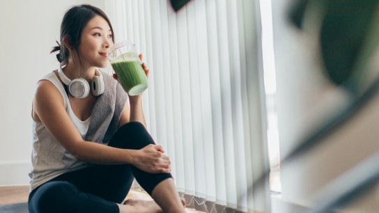 Beautiful young Asian woman in sportswear drinking protein shake after exercise, relaxing at home.