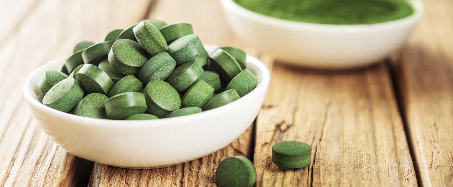 Tablets of chlorella or spirulina in white cups on a wooden background.