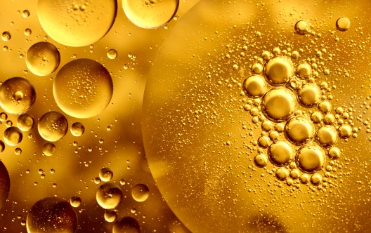 Full frame macro photography of gold-colored water and oil, forming an abstract pattern of circles and bubbles.