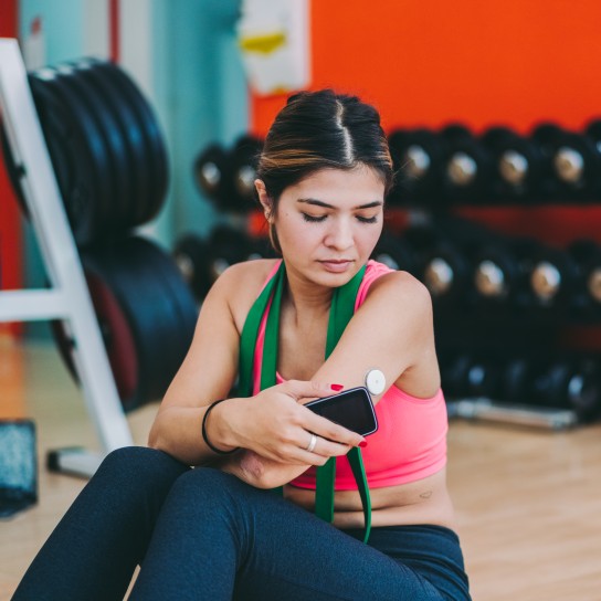 Young woman with diabetes is wearing small sensor on the back of upper arm for controlling blood sugar. She is scanning the sensor with smartphone for checking test results on phone