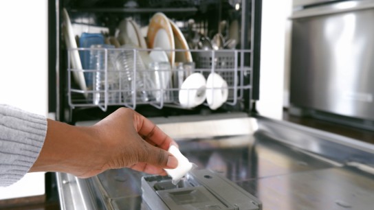 Close-up of black woman's hand putting dishwasher detergent pod into dispenser