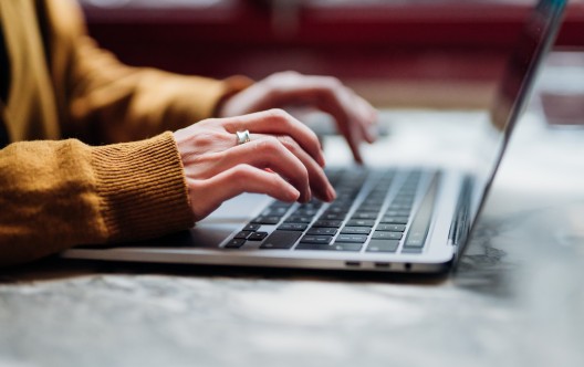 Side view of female hand typing on laptop keyboard. Freelancer working with laptop at cafe. Technology and flexible working.