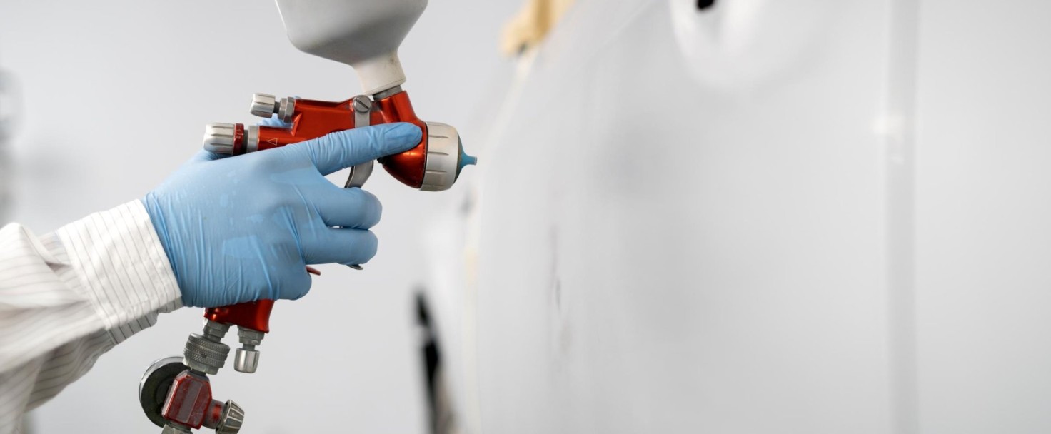 Close-up image of car painter with protective clothes and mask painting car using spray compressor in Auto Repair Shop.