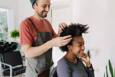 Photo of a young smiling hairdresser, serving a customer with an Afro hair