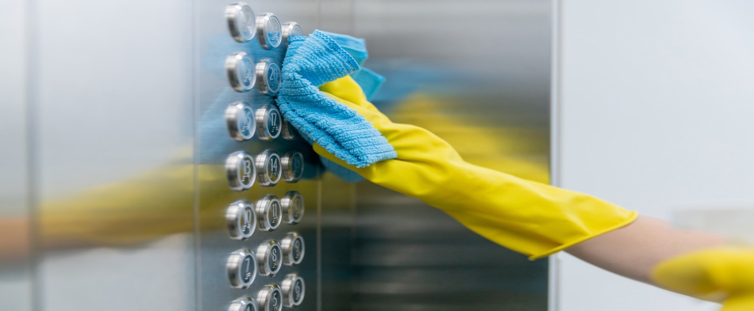 Close-up on a cleaner cleaning the buttons of an elevator in a building using gloves and a wet cloth