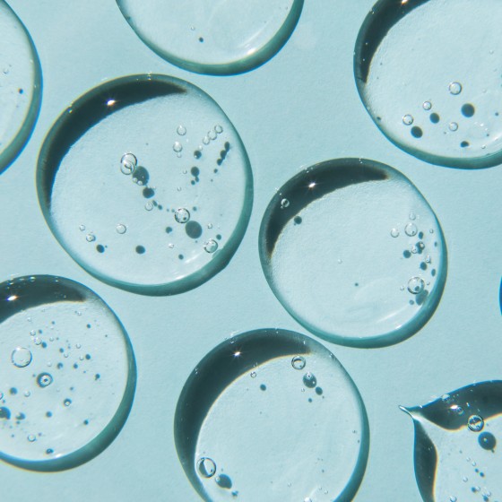 Drops of natural moisturizing gel on blue background. Flat lay, top view. Skincare beauty product