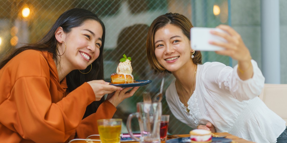 Female friends are enjoying eating sweet food in cafe and sharing their time on social media with a smart phone.