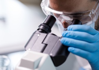 Copy space shot of laboratory tech, in protective gear, looking through the microscope and analyzing scientific samples.