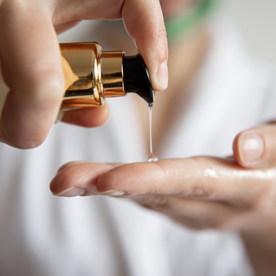 Close-up, a woman in a white robe presses on the dispenser of beauty care products, blurred background.