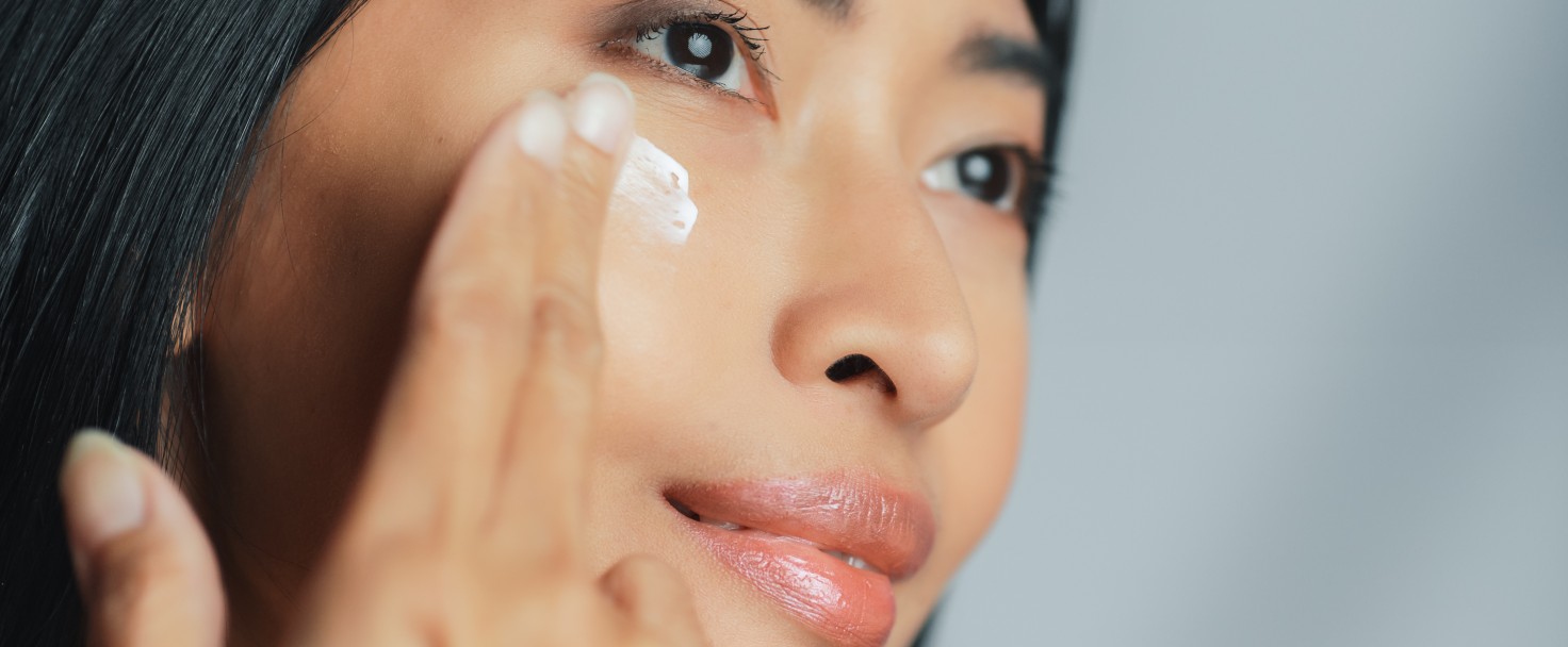 Beautiful Asian Woman Gently Touching Her Face, Looking Away. Young Adult Female with Lush Black Hair Makes Her Skin Soft, Clean with Natural Cosmetics Skincare Product. Close-up Portrait