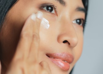 Beautiful Asian Woman Gently Touching Her Face, Looking Away. Young Adult Female with Lush Black Hair Makes Her Skin Soft, Clean with Natural Cosmetics Skincare Product. Close-up Portrait