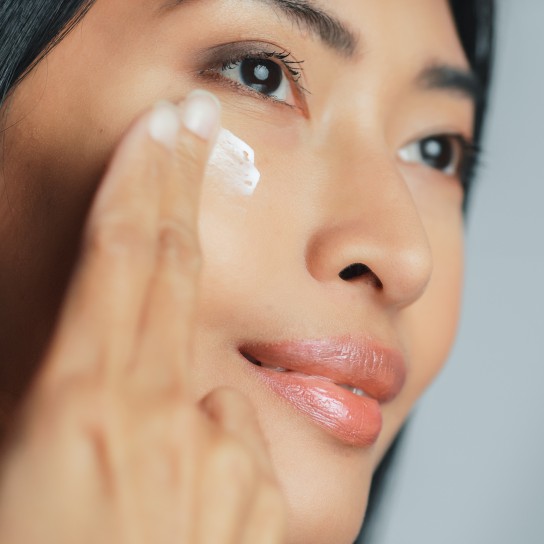 Beautiful Asian Woman Gently Touching Her Face, Looking Away. Young Adult Female with Lush Black Hair Makes Her Skin Soft, Clean with Natural Cosmetics Skincare Product. Close-up Portrait